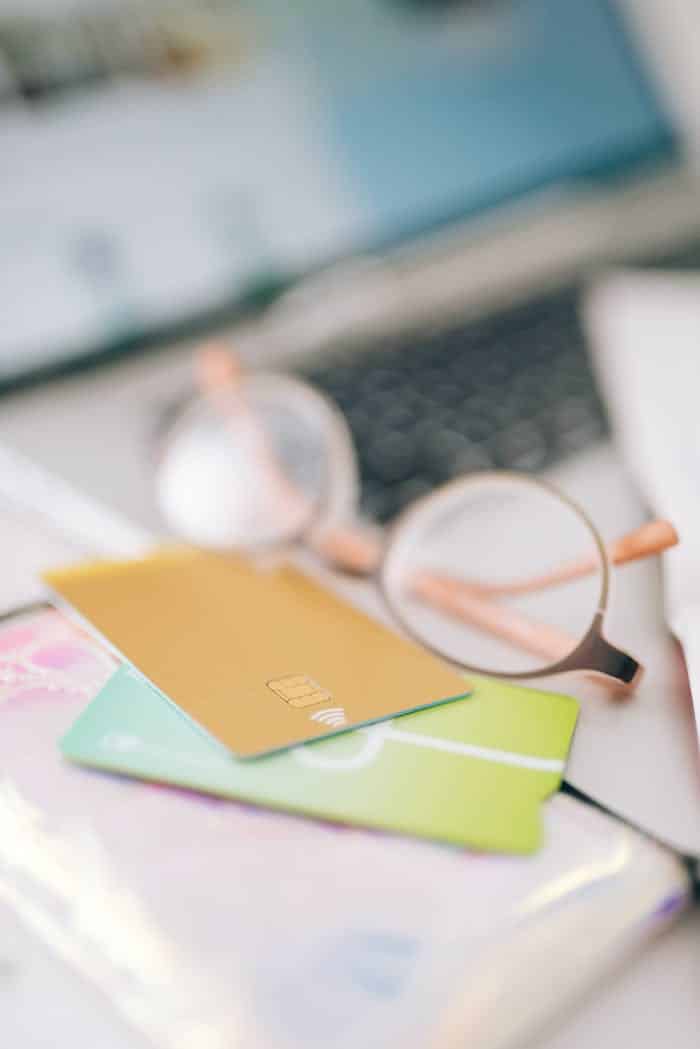 Qui sommes-nous? Blurred close-up of credit cards, eyeglasses, and laptop on a desk, evoking online shopping theme.